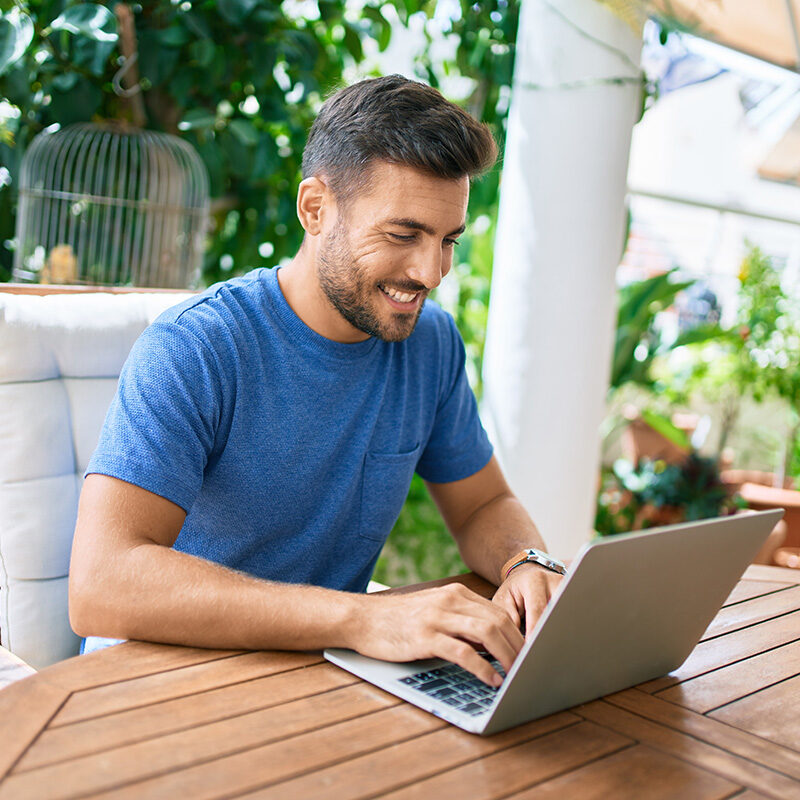 Young hispanic man working using laptop at the terrace.